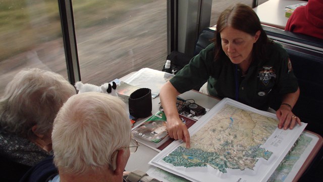 In a train car where an instructor leads two passengers through a tactile exploration of map.rati