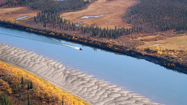 View from the sky of boat on river with surrounding fall foliage 