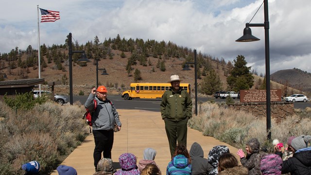 A park ranger talking to a school group with a yellow bus in the background.