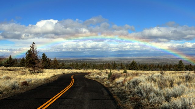 A road winding off into the distance with a rainbow across the sky.