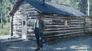 a man stands next to a wood cabin