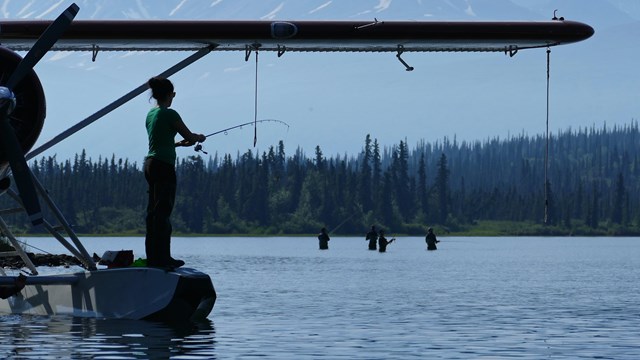 A person fishes while standing on the float of a seaplane