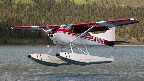 A red and white floatplane takes off from a lake