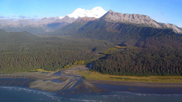 photo of a snow-capped volcano towering over the ocean and foothills.