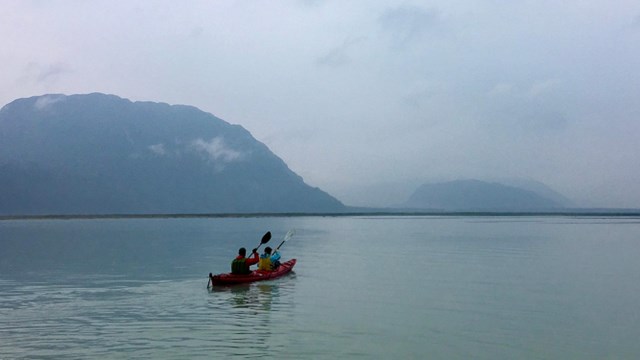Landscape view of a kayak with two paddlers out on the water with mountains in the distance.