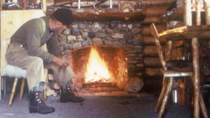Image of a man in front of a fireplace in a log cabin.