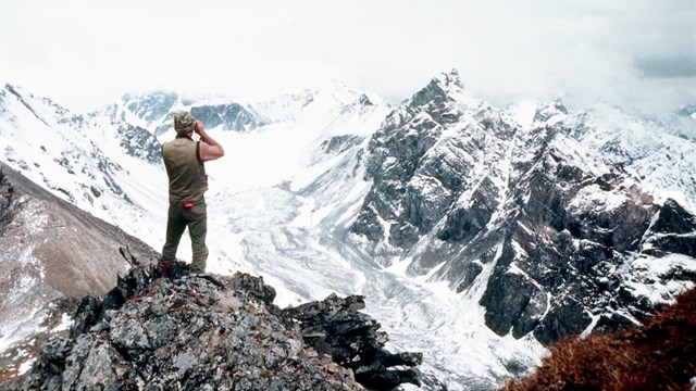 Vintage photo of a man looking across a glaciated mountain valley with binoculars.