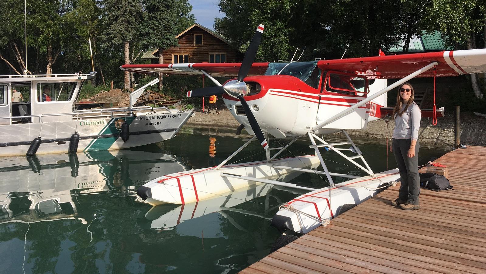 a woman stands on a dock next to a plane and a boat