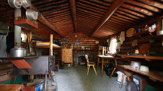 Photo of the interior of a small, one room log cabin filled with rustic items..