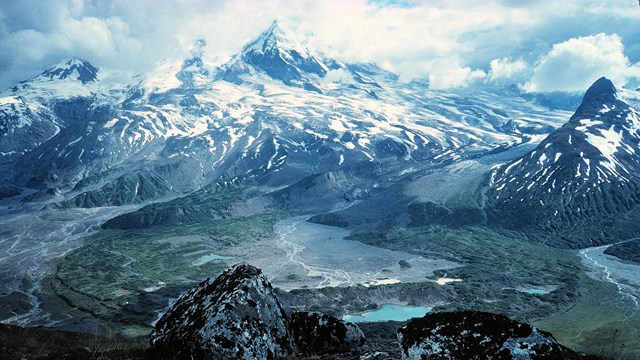 photo of a glaciated volcano with alpine tundra and a river valley in the foreground.