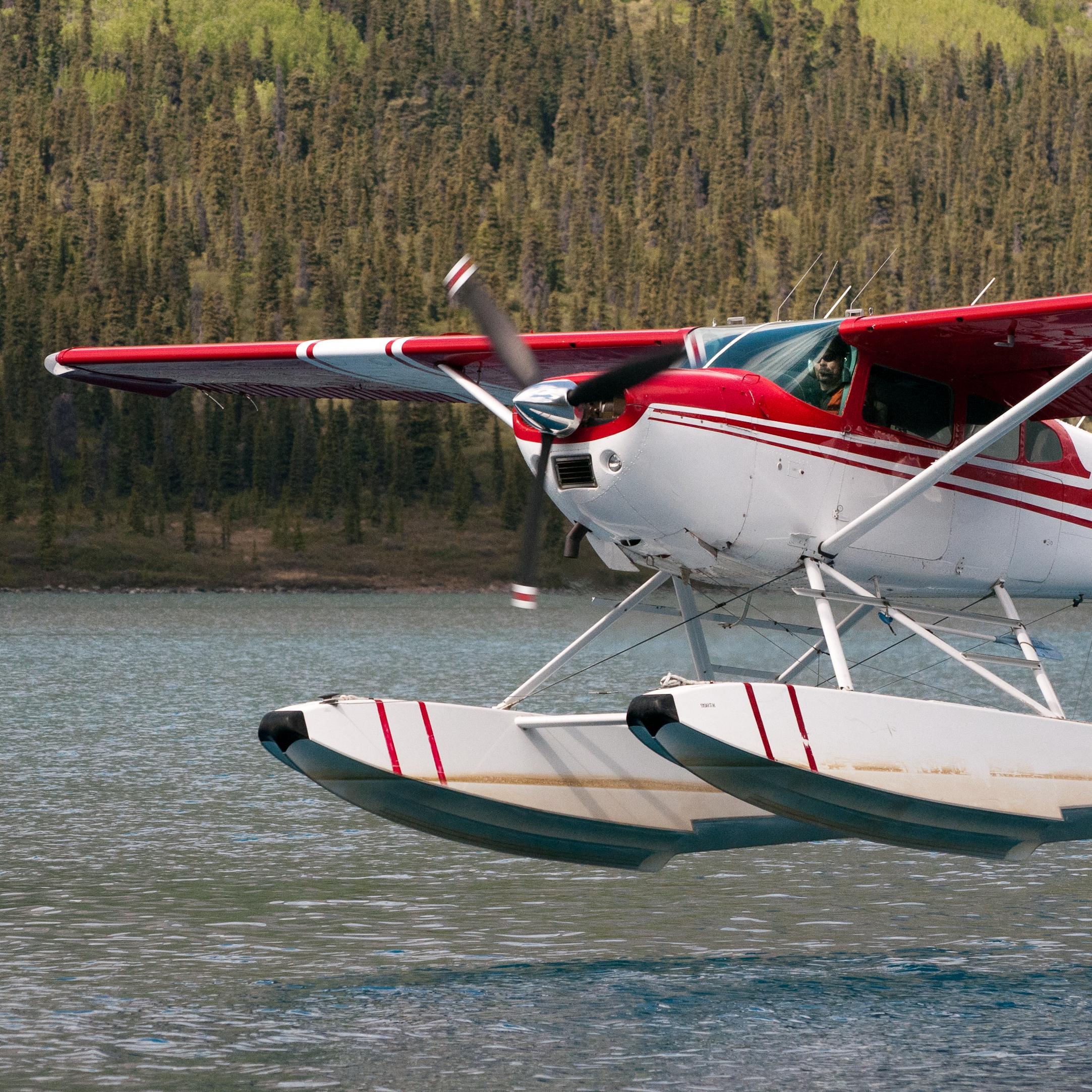 A red and white floatplane takes off from a lake