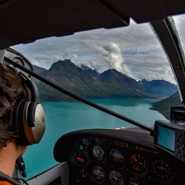 Float plane landing on a blue lake surrounded by steep mountains.