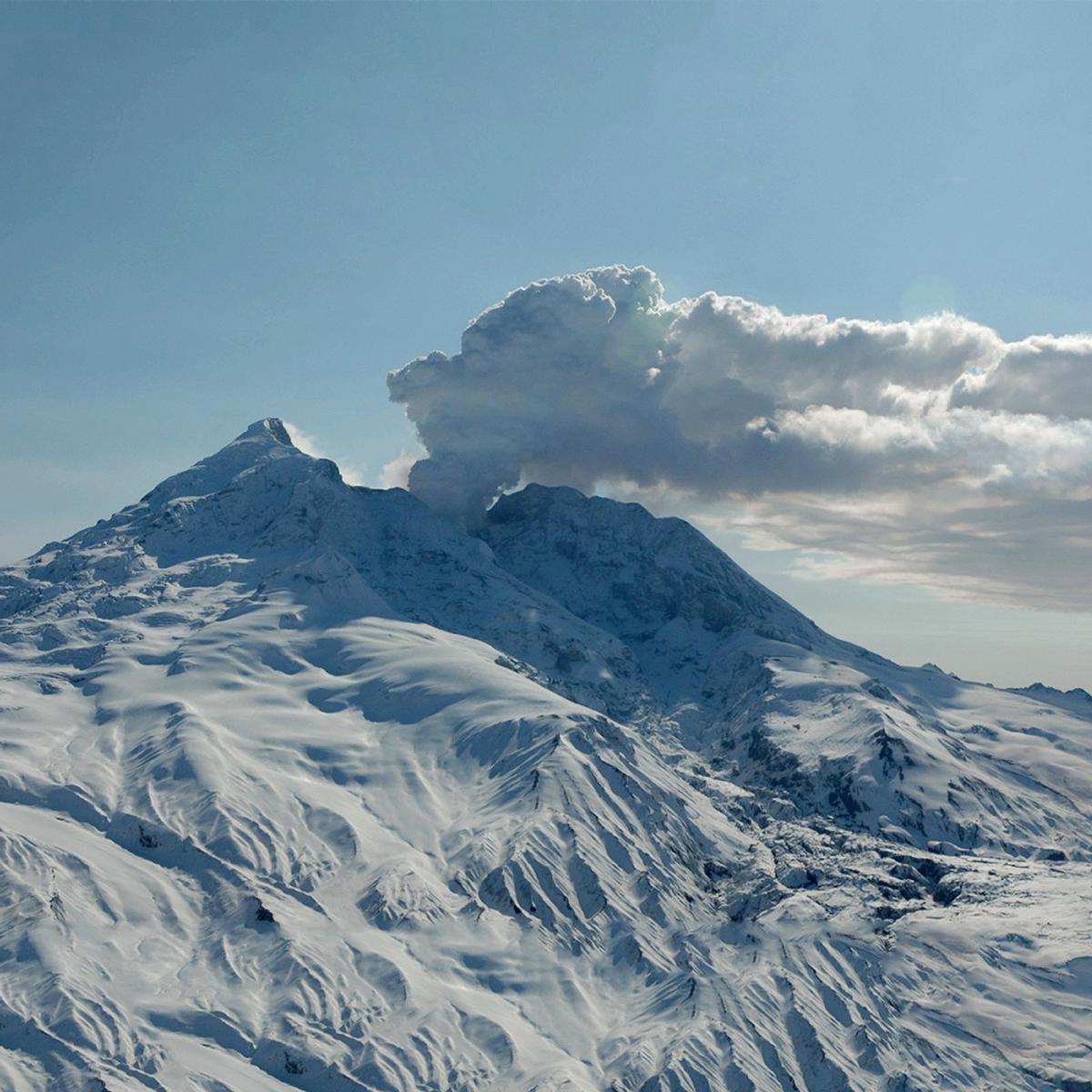 A plume of steam rises from a snow and ice-capped volcano on a clear day. Photo by Dennis Anderson.