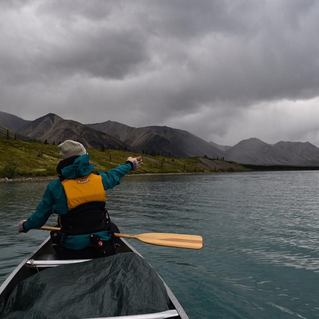 a woman in a canoe points towards a storm ahead