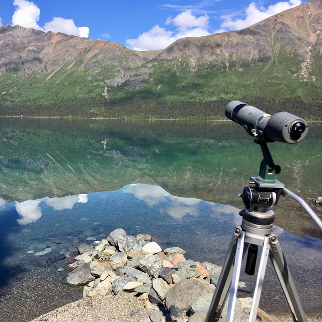 a spotting scope pointed at a mountain that is reflecting in a lake