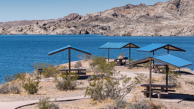 Several singular picnic table shelters next to a large body of water.