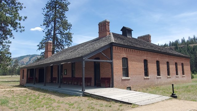 Brick building with a black pointed roof and a long porch.