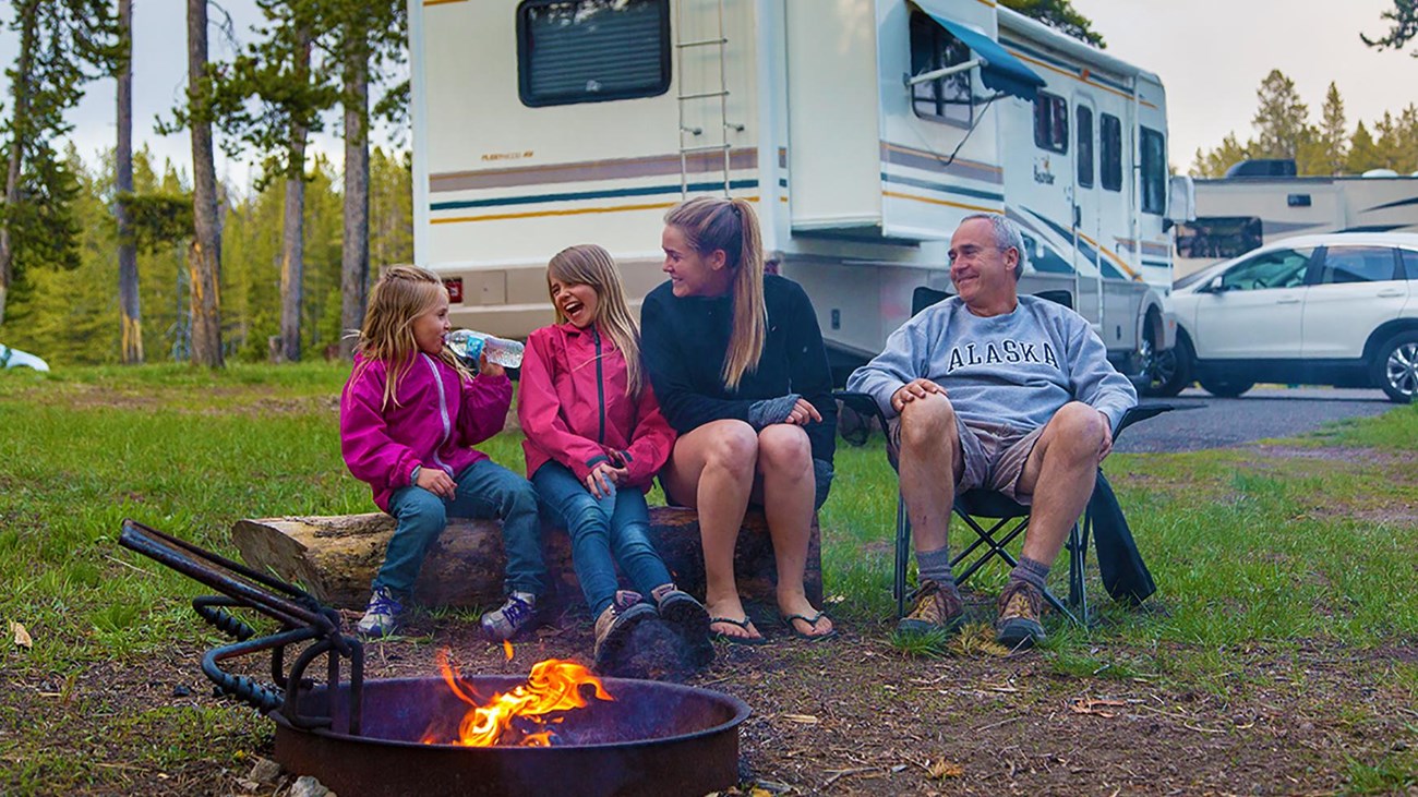 A family enjoying a camping trip, sitting by a campfire near their RV.