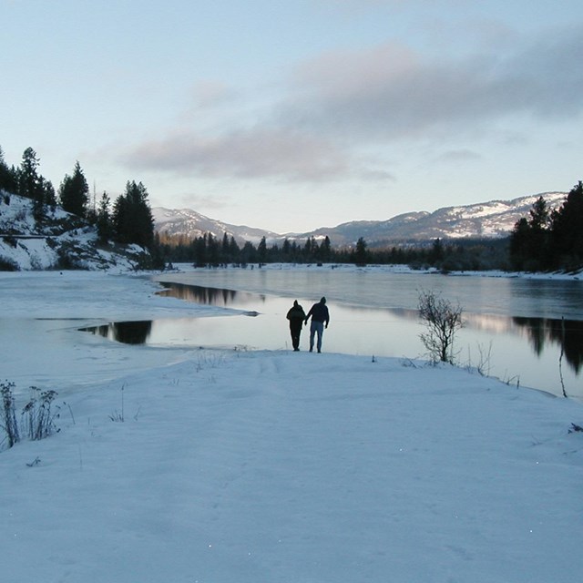 Two people wandering the snowy shoreline of the lake in winter.