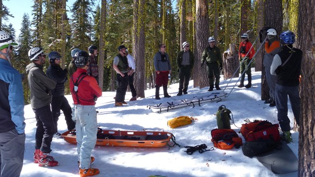 group standing around a bright orange litter in a snowy wooded area