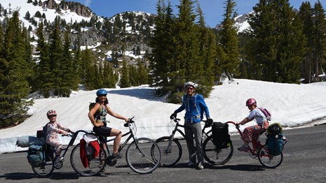A family on two bikes poses for a photo on a highway backed by snow