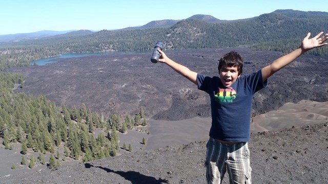 a boy raising his arms above his head in excitement at a large cinder field behind him