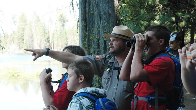 a ranger points into the distance, kids and adults look on with binoculars