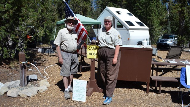 two camp hosts in uniform standing in front of their campsite