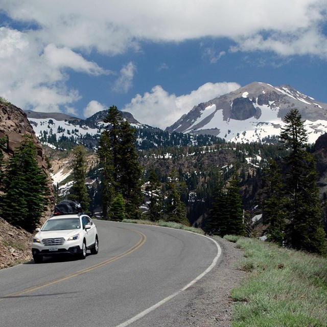 A white vehicle on a highway backed by a snow-covered volcano