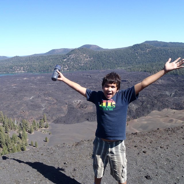 a boy raising his arms above his head in excitement at a large cinder field behind him