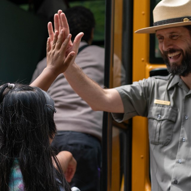 Girl high-fives with a park ranger before boarding school bus.