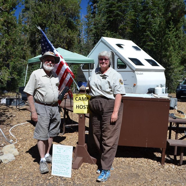 two camp hosts in uniform standing in front of their campsite