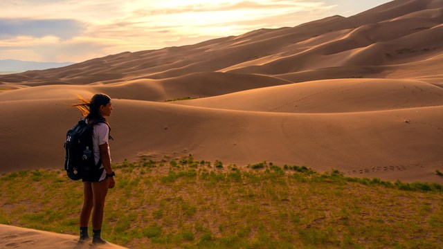 Young woman standing at edge of sand dunes at sunset