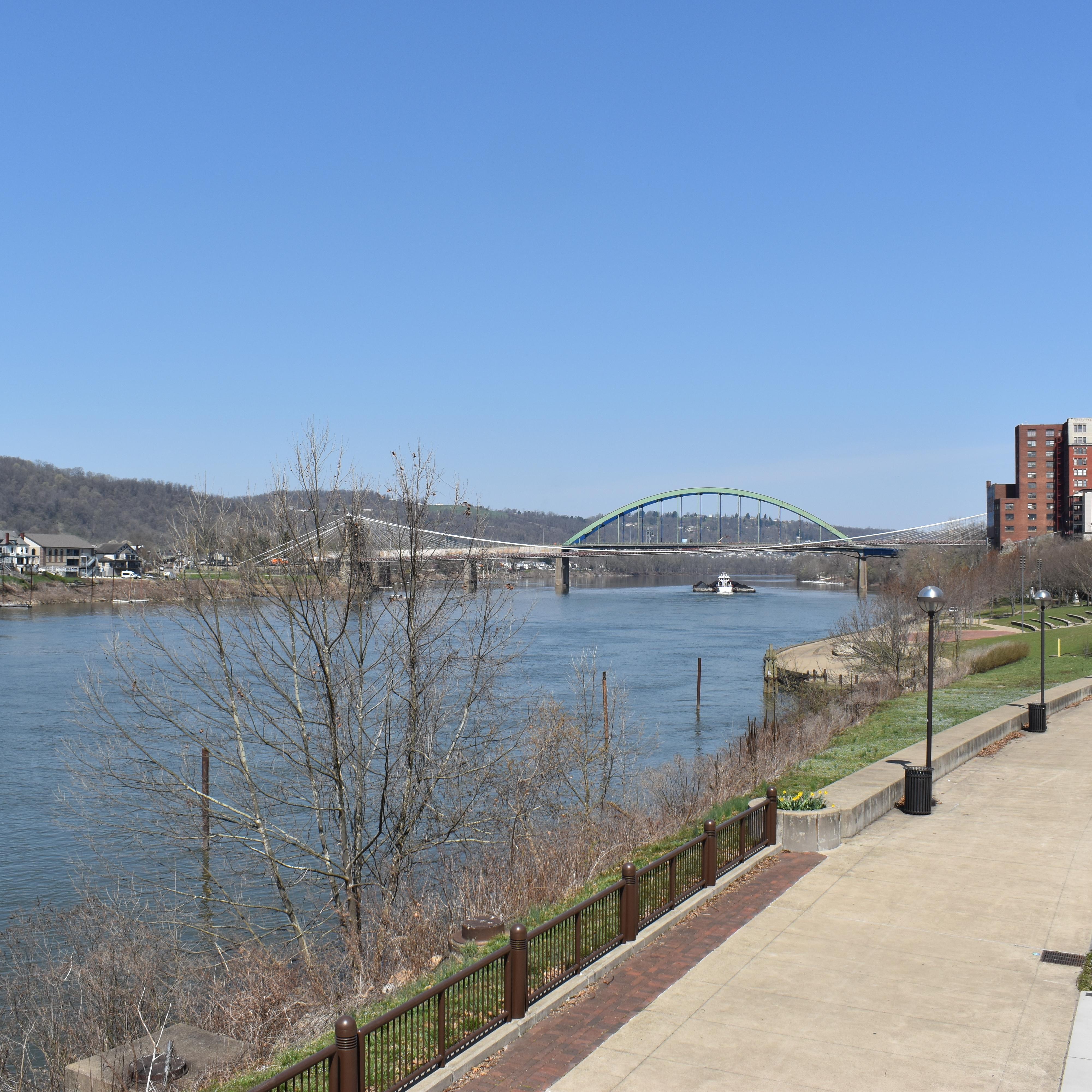 paved walking path near river with bridge in view