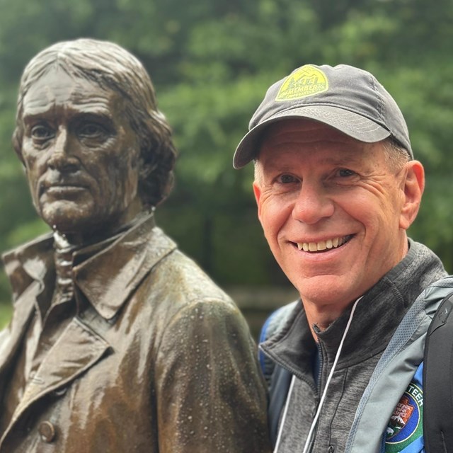 man in a cap next to a statue of a man