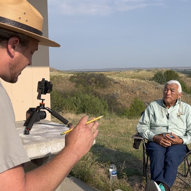a man in a park ranger uniform interviews a man with braided hair