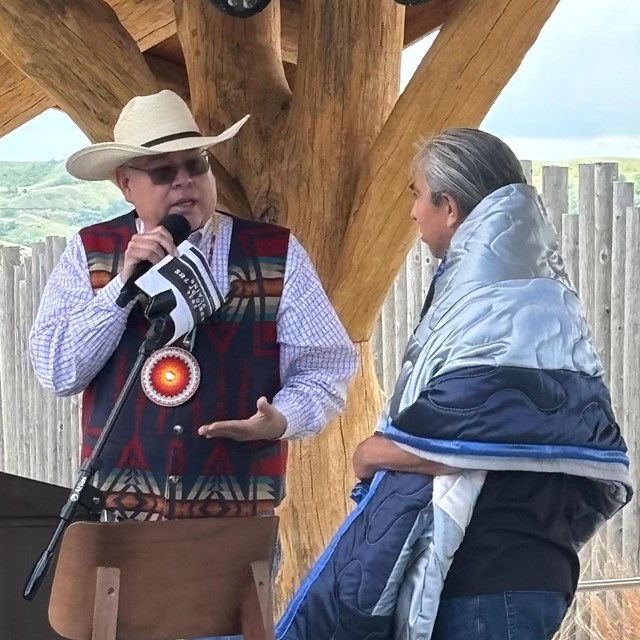 a man wrapped in a blanket looks at a man holding a microphone