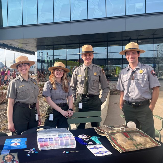 four people in park ranger uniforms stand behind an informational booth
