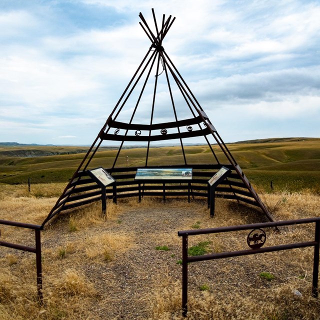 Teepee frame stands in grassy plains.