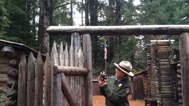 Ranger holding stuffed bison in front of Fort Clatsop