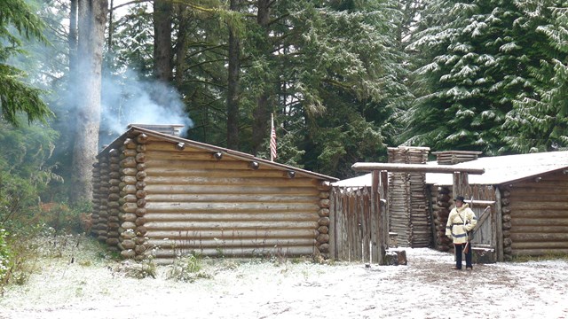 Fort Clatsop with smoke coming from a vent, snow covering the roof and ground outside.