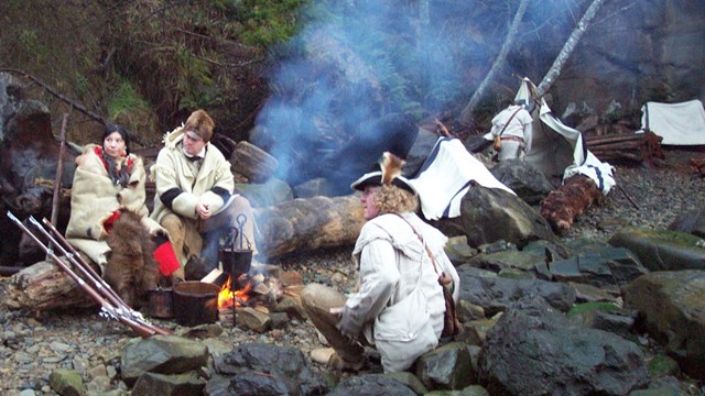 Actors dressed as members of the Lewis and Clark expedition sit by a fire along the Columbia River.