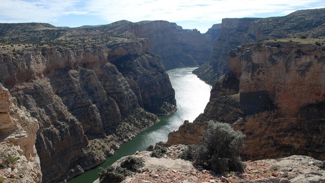 a river in sunlight below vertical sandstone cliffs