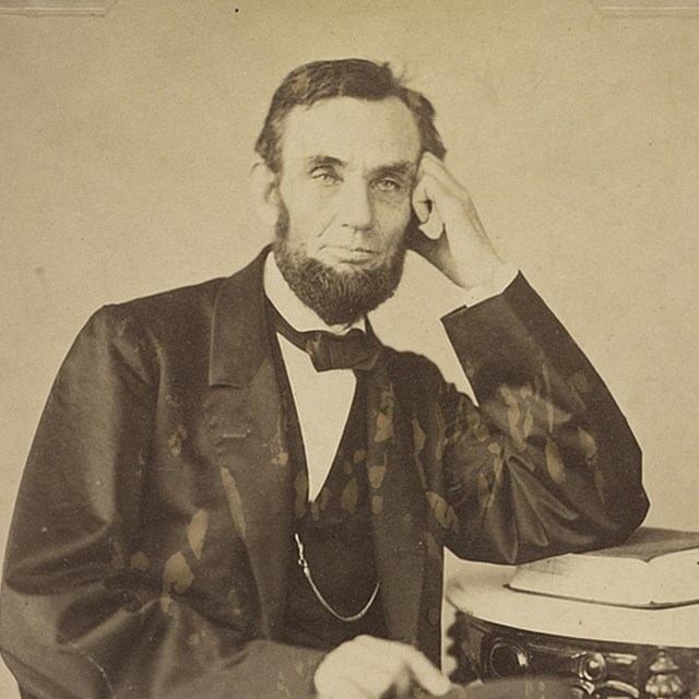 Abraham Lincoln in 1863, bearded and leaning against table
