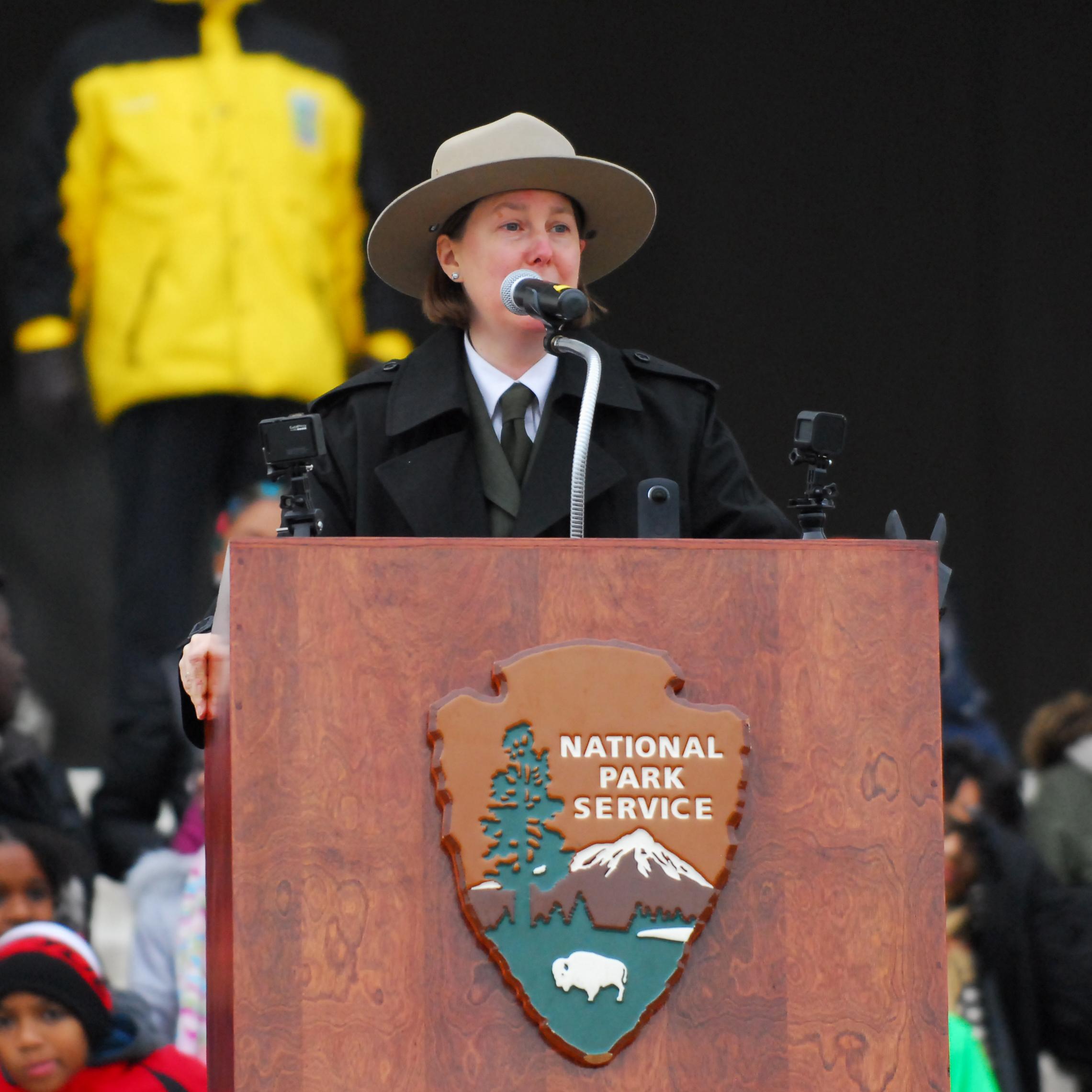 A ranger in uniform speaks at a podium on the steps of the Lincoln Memorial.