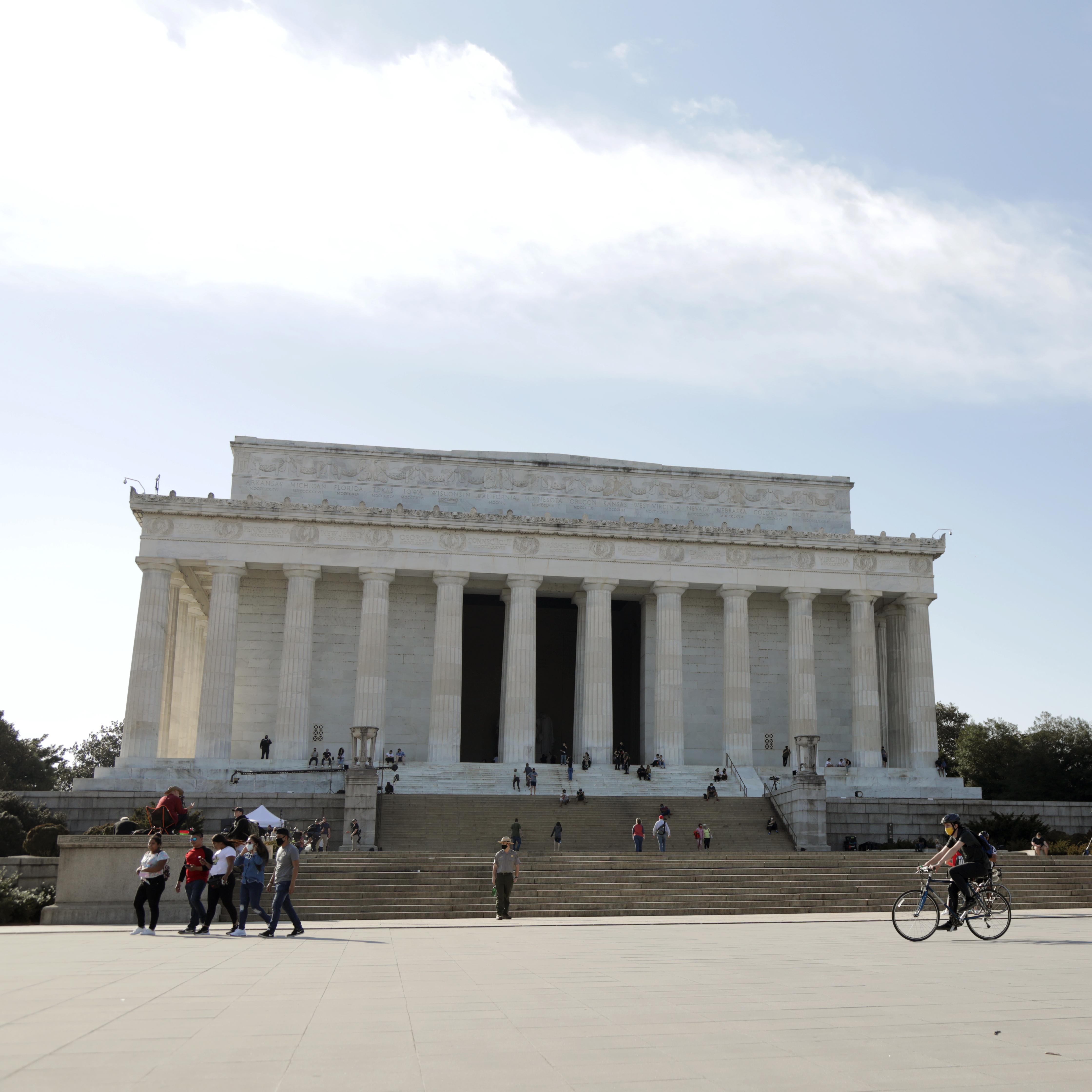 Visitors bike and walk in front of the steps of the Lincoln Memorial.