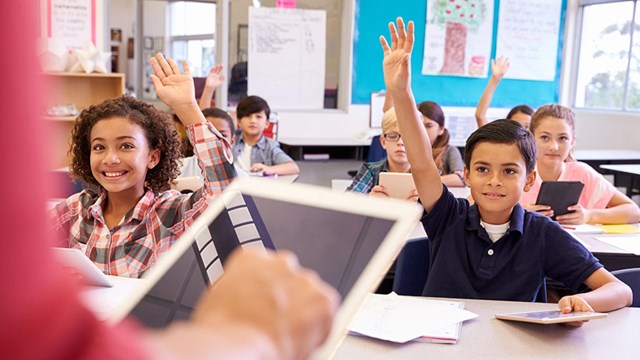 Young students in aq classroom raise their hands