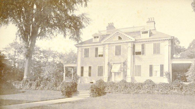 Black and white image of front of mansion with lawn in foreground