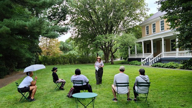 Ranger with five visitors seated on the east lawn of the Longfellow House.