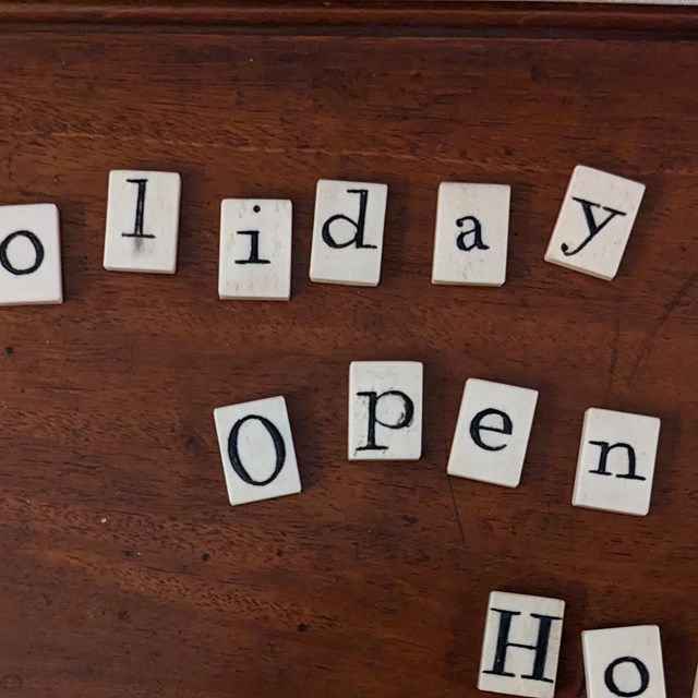 Tiles from a 19th century word game spell out Holiday Open House; on top of a wooden box